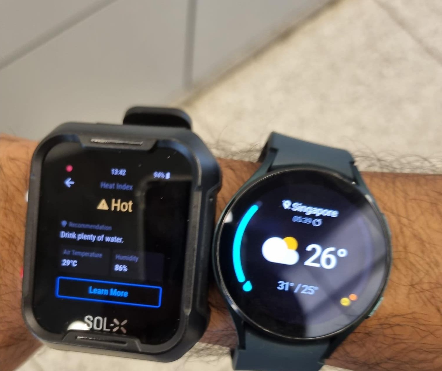 The previous SOL-X heat alert worn alongside a standard smartwatch, comparing heat index, humidity and hydration guidance against generic weather